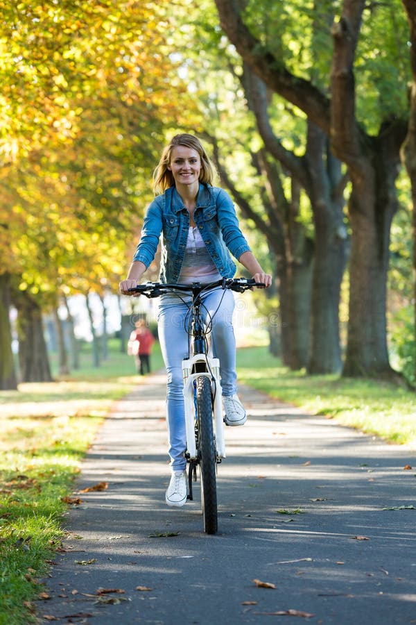 Young woman ride bike in autumn park. Enjoying while cycling in nature during autumn day