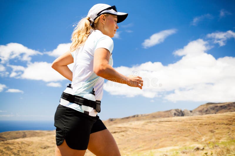 Young woman running in mountains on sunny summer day. Female runner exercising outdoors in nature, sunset.