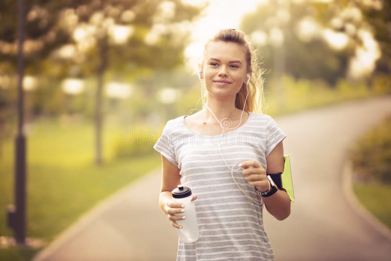 Young woman running in park and listening to music with headphones - Beautiful blonde and fit girl jogging alone outdoor in early royalty free stock photos Young woman running in park and listening to music with headphones - Beautiful blonde and fit girl jogging alone outdoor in early royalty free stock photos