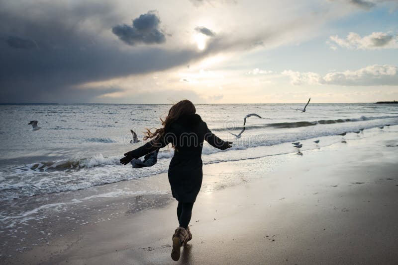 Young woman runs along the coast of the ocean behind the birds.