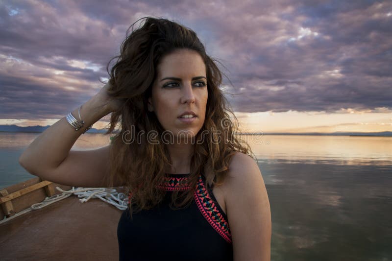 Young woman sailing in a boat on a cloudy day looking at the horizon while she is grooming her hair stock photography Young woman sailing in a boat on a cloudy day looking at the horizon while she is grooming her hair stock photography