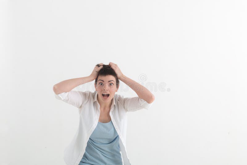 Young woman screaming in terror with hands on her head, mouth wide open looking in panic at the camera. Close up portrait of irritated female shouting, covering her ears, angry with noisy neighbours.