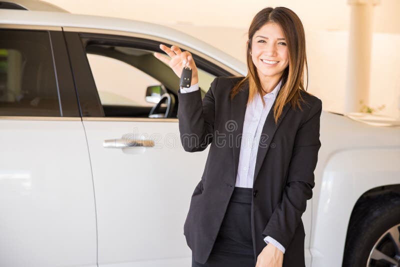 Attractive young brunette in a suit handing over the keys to your new car and smiling. Attractive young brunette in a suit handing over the keys to your new car and smiling