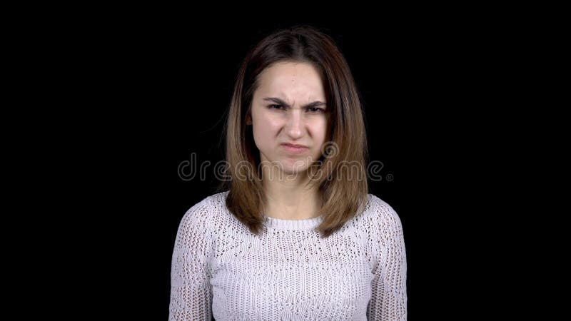 A young woman shows disgust emotions on her face. Woman contorts her face from abomination on a black background.