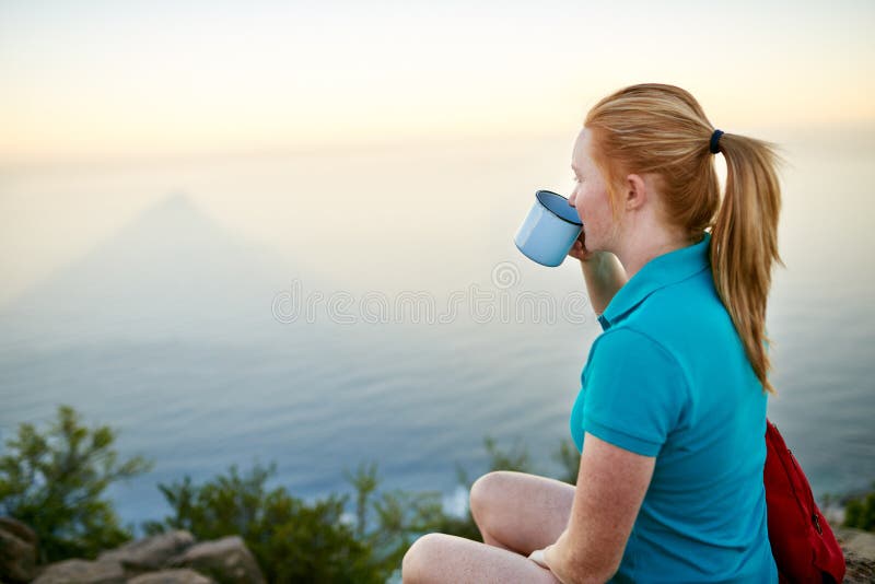 Young woman on an early morning hike quietly sipping her coffee and taking in the view. Young woman on an early morning hike quietly sipping her coffee and taking in the view