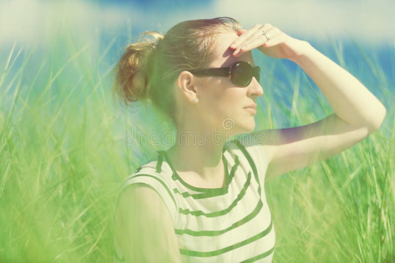 Young woman sitting in sand dunes amongst tall grass relaxing, enjoying the view on sunny day