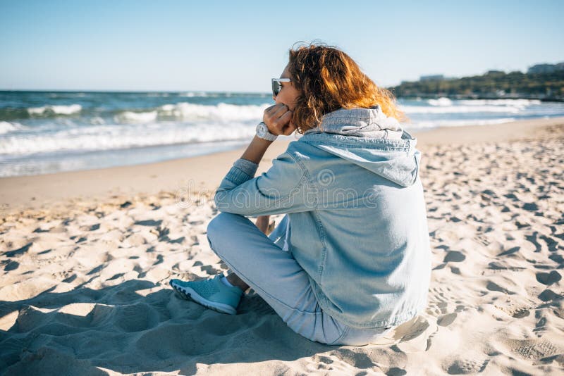 Young woman sitting on sandy beach looking at waves stock images Young woman sitting on sandy beach looking at waves stock images