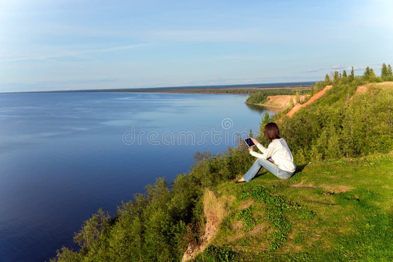 Young woman sitting on the shore of the lake with tablet compute stock photography Young woman sitting on the shore of the lake with tablet compute stock photography