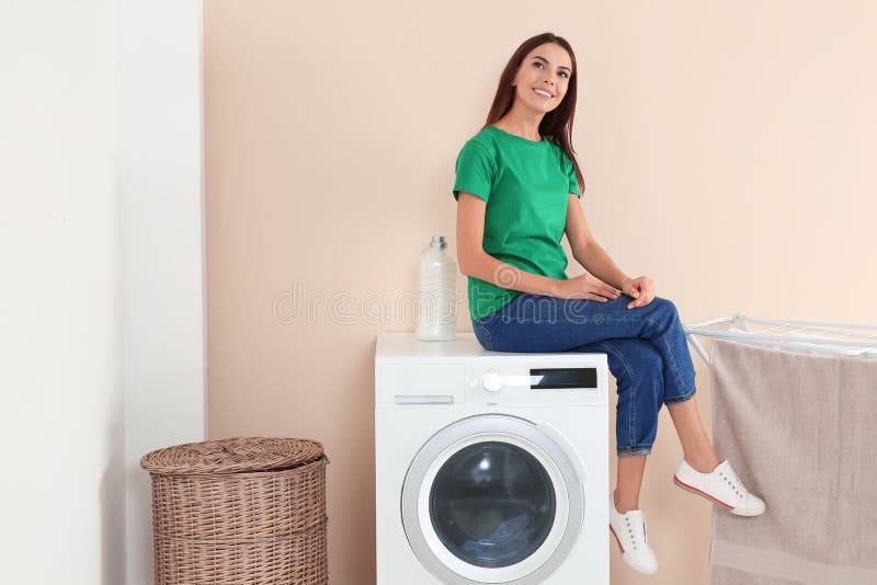 Young woman sitting on washing machine at home. 