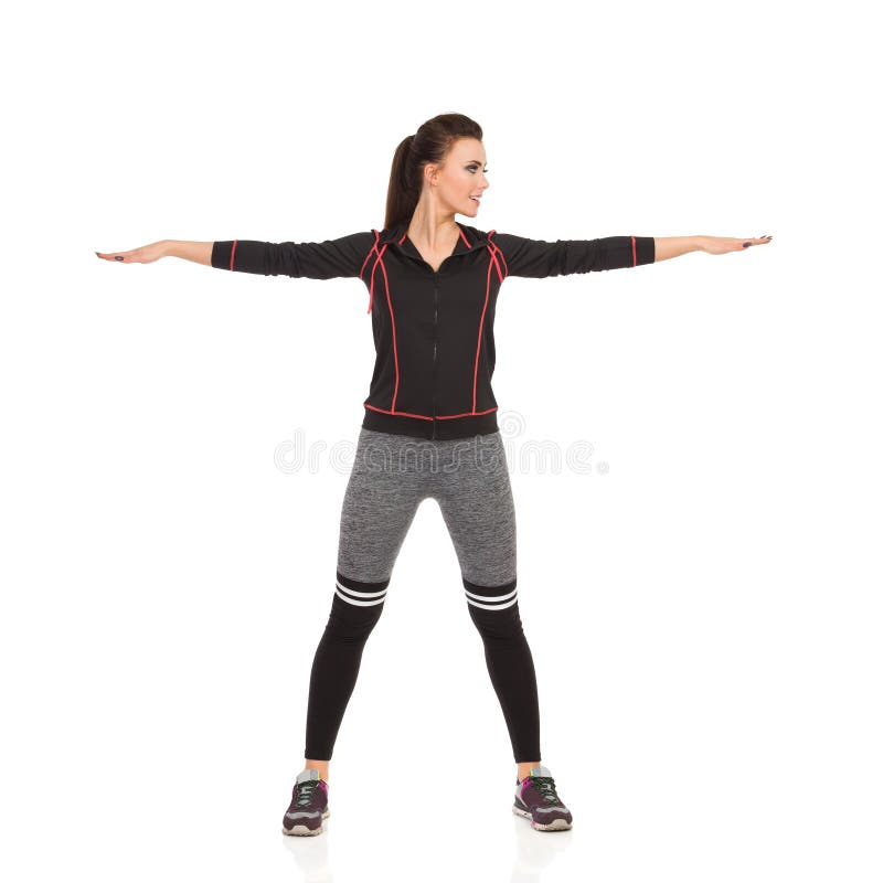 Young Woman In Sports Clothes Is Standing With Arms Outstretched. Beautiful young woman in fitness clothes is standing legs apart, holding arms outstretched and royalty free stock photography Young Woman In Sports Clothes Is Standing With Arms Outstretched. Beautiful young woman in fitness clothes is standing legs apart, holding arms outstretched and royalty free stock photography