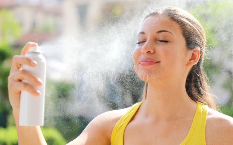Young woman spraying Thermal Water on her face outside. Thermal water used for skin care, fix makeup, help skin irritation