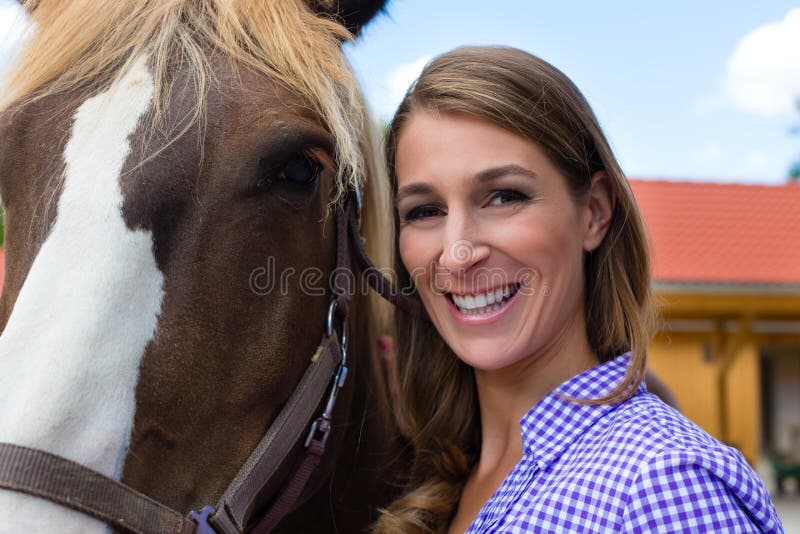 Young woman in the stable with horse in sunshine