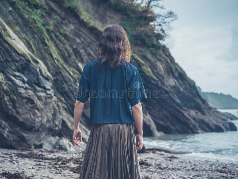 A young woman is walking on the beach and is looking at a cliff. A young woman is walking on the beach and is looking at a cliff