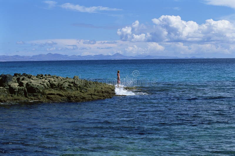 Young woman standing on rocks, looking out to sea