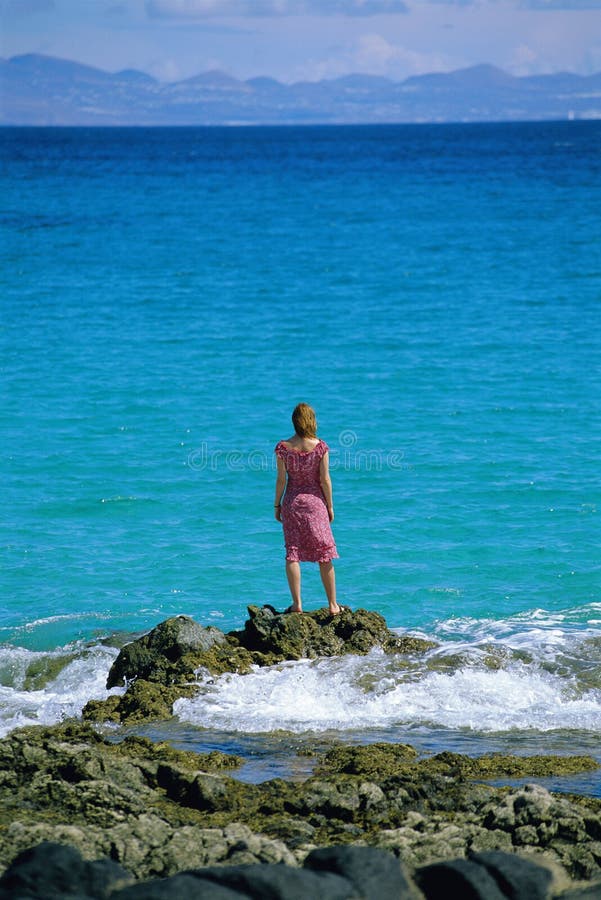 Young woman standing rocks, looking out to sea