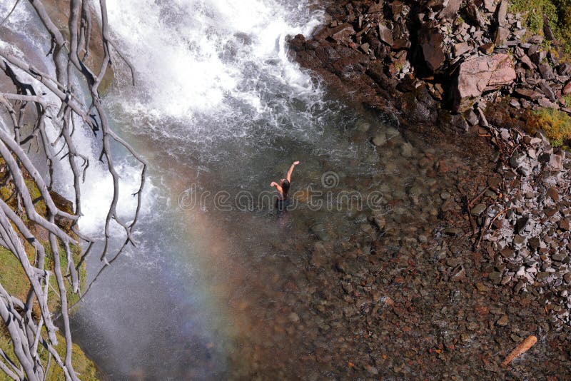 A young woman standing in a waters of Tumalo falls stream with hand up and spread apart.