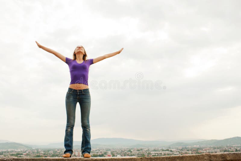 Young woman staying with raised hands against blue sky