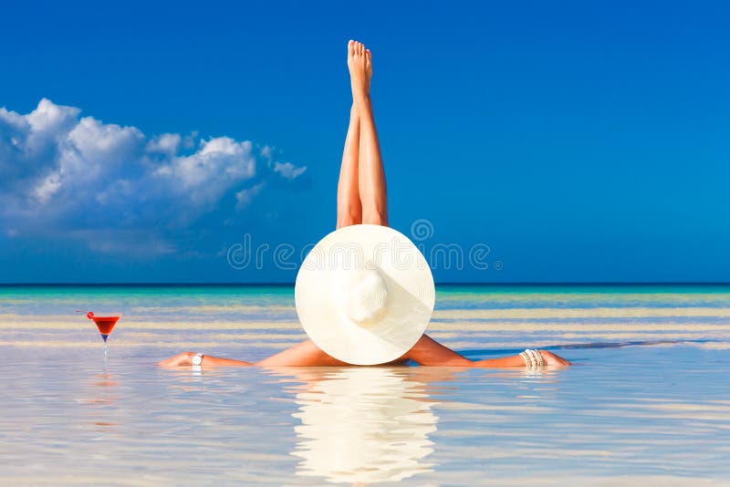 young woman in straw hat laying at the tropical beach and enjoying cocktail