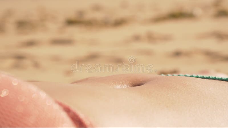 Young woman sunbathing on sandy beach, closeup detail to her belly moving up and down as she breathers