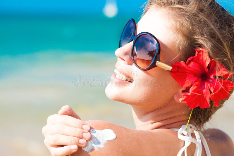 Mujer joven en gafas de sol introducción el sol crema sobre el hombro.