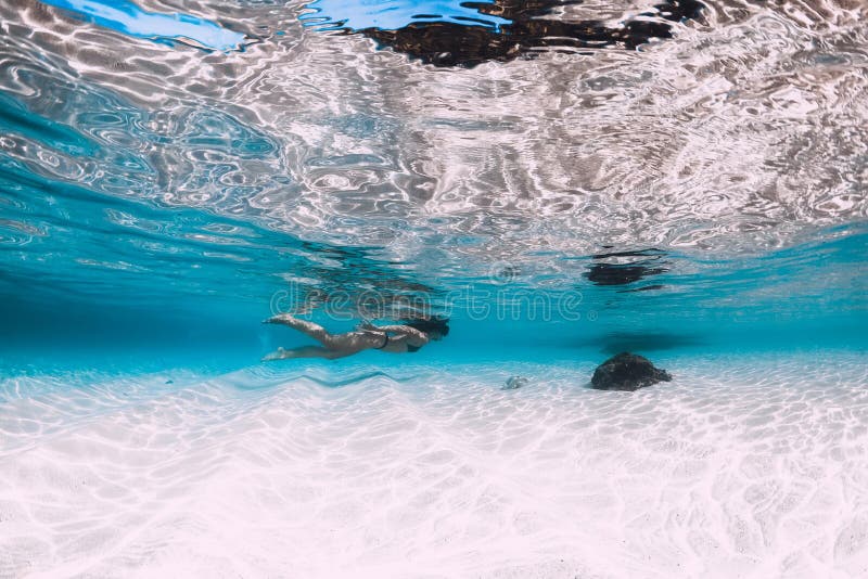 Young woman swimming underwater in the tropical blue ocean with sand stock photography Young woman swimming underwater in the tropical blue ocean with sand stock photography