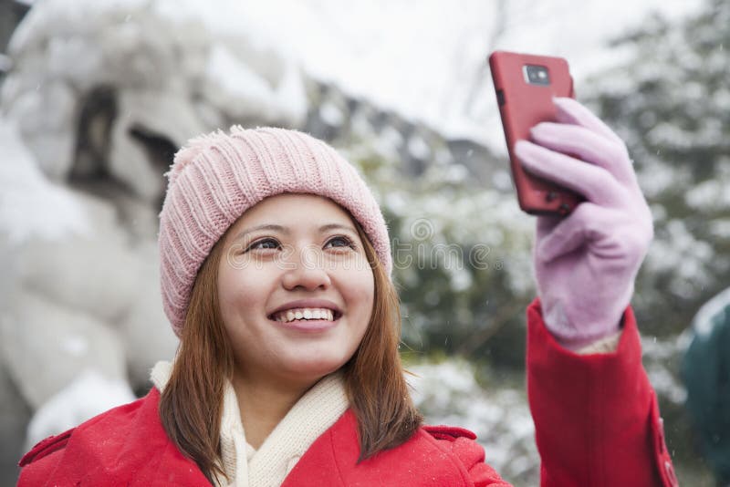 Young woman taking picture with cell phone in snow