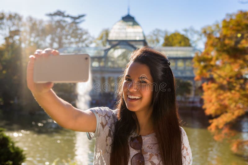 Close up portrait of attractive female making selfie, using selfie stick,  poses, takes photo for her social network, makes surprised look, stands  with open mouth, keeps hand on cheek. Teen concept. Stock