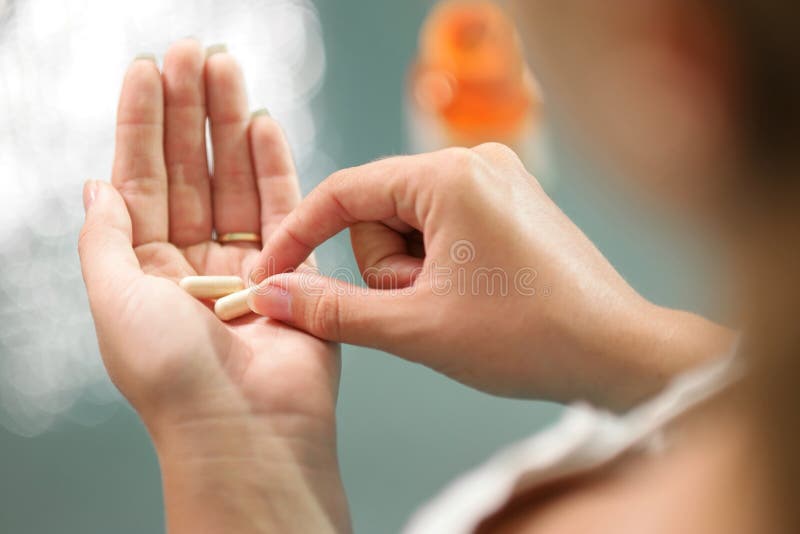 De cerca de mujer joven posesión cosecha vitaminas a minerales pastillas en la mano una botella sobre el mesa.