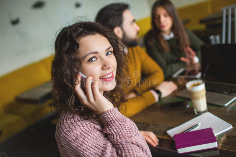 Young woman talking phone with happy friends in cafe