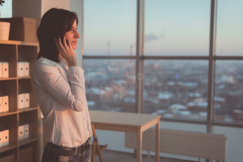 Young woman talking using cell phone at office in the evening. Female businesswoman concentrated, looking forward