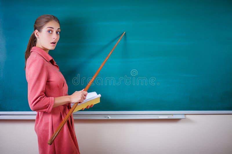 Young woman teacher stands at a blackboard with a pointer. Template for the school timetable and other information. Beautiful tacher shows on empty copy space on the school board. Education concept