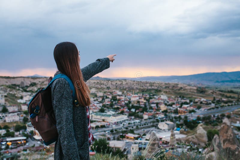 Young woman tourist with high point showing hand at sunset over the city of Goreme in Turkey. Cappadocia. Tourism, rest