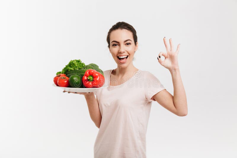 young woman with tray of various fresh vegetables showing okay sign