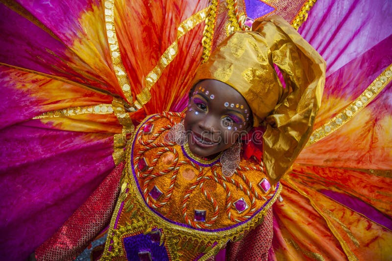 A young woman in Trinidad Carnival masquerade. A brightly clad masquerader in pink, gold and orange with a richly designed color smiles with great joy as she stock image A young woman in Trinidad Carnival masquerade. A brightly clad masquerader in pink, gold and orange with a richly designed color smiles with great joy as she stock image