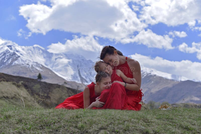 A young woman with two daughters in red dresses resting in the snow-capped mountains in the spring. stock photography A young woman with two daughters in red dresses resting in the snow-capped mountains in the spring. stock photography
