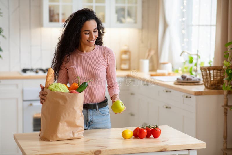 Young Woman Unpacking Paper Bag With Vegetables And Fruits After Grocery Shopping