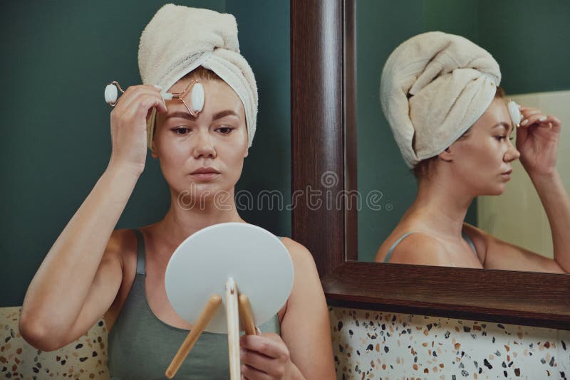 Young Woman Using Jade Facial Roller For Face Massage Sitting In