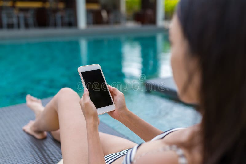 Young Woman using mobile phone and lying besides swimming pool ,Asian young woman
