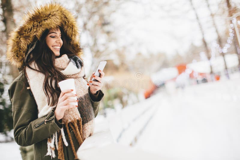 Young woman using a phone and drinking hot tea in the winter par royalty free stock photos Young woman using a phone and drinking hot tea in the winter par royalty free stock photos