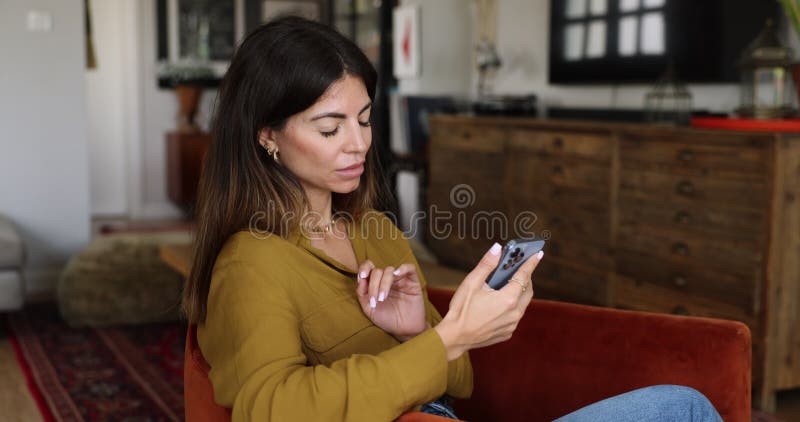 Young woman using smartphone seated in armchair in living room stock footage