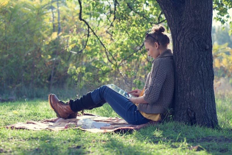 Lumbar estilo mujer joven ordenador personal durante Descansar un árbol.