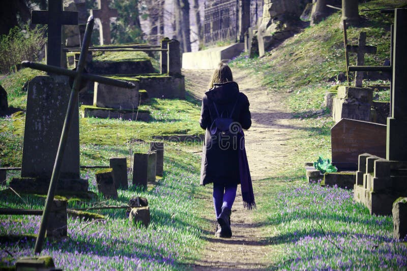Young woman walking on cemetery path between grave stones and crosses in spring stock photography Young woman walking on cemetery path between grave stones and crosses in spring stock photography