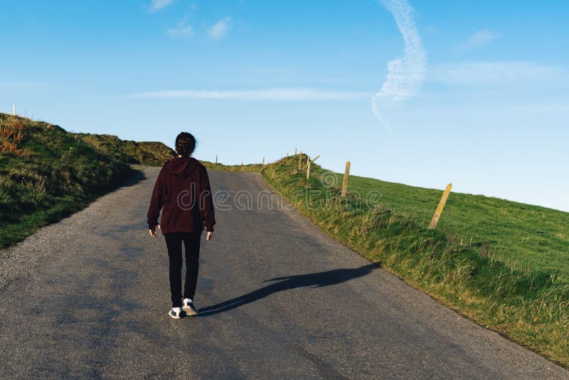 Young Woman Walking On Lonely Road Next To Green Fields Stock Image