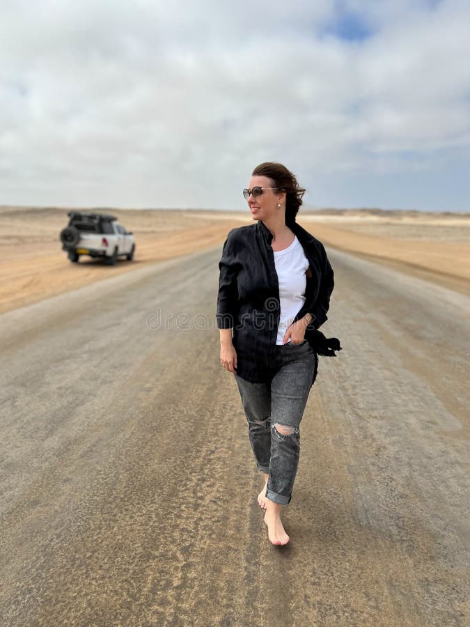 Young woman walks on highway in desert. Travel Africa, Namibia. Girl on center of the road, barefoot. Skeleton coast asphalt. Young woman walks on highway in desert. Travel Africa, Namibia. Girl on center of the road, barefoot. Skeleton coast asphalt.