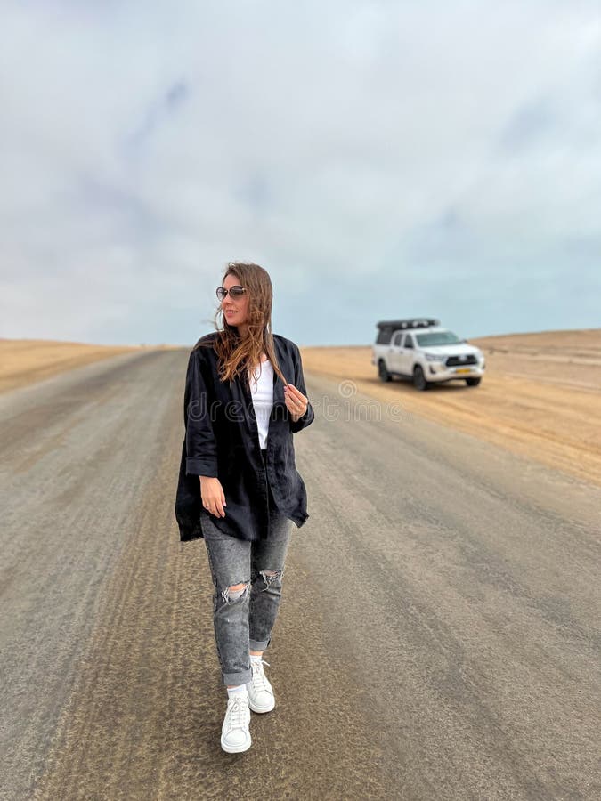 Young woman walks on highway in desert. Travel Africa, Namibia. Girl on center of the road, barefoot. Skeleton coast asphalt. Young woman walks on highway in desert. Travel Africa, Namibia. Girl on center of the road, barefoot. Skeleton coast asphalt.