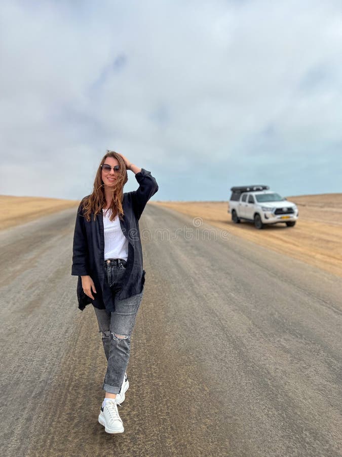 Young woman walks on highway in desert. Travel Africa, Namibia. Girl on center of the road, barefoot. Skeleton coast asphalt. Young woman walks on highway in desert. Travel Africa, Namibia. Girl on center of the road, barefoot. Skeleton coast asphalt.