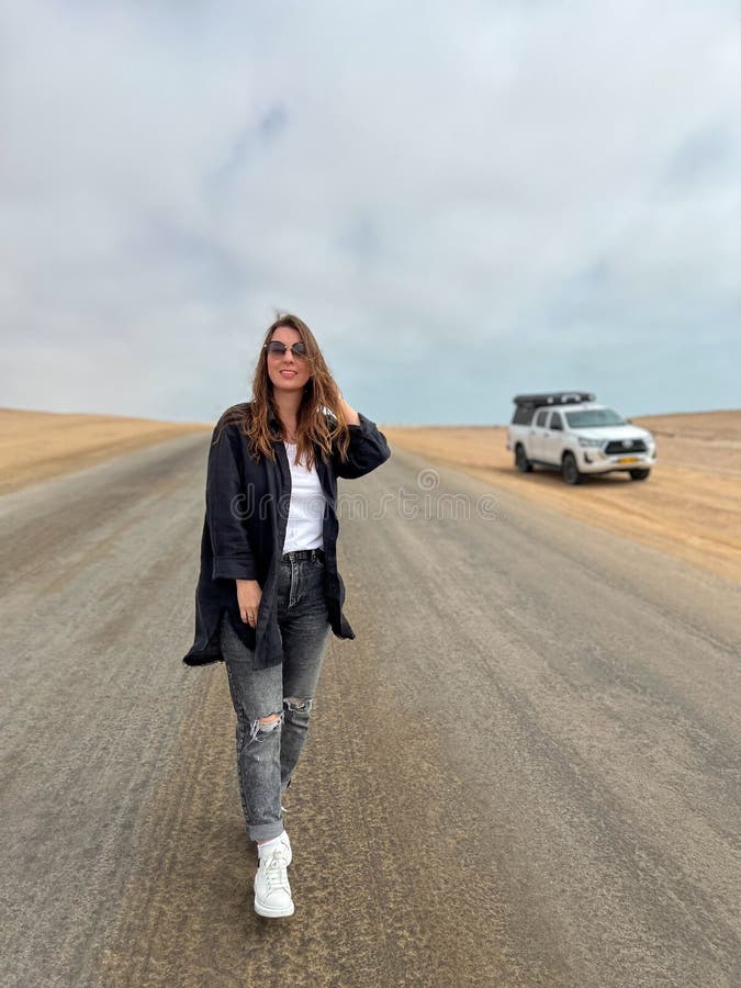 Young woman walks on highway in desert. Travel Africa, Namibia. Girl on center of the road, barefoot. Skeleton coast asphalt. Young woman walks on highway in desert. Travel Africa, Namibia. Girl on center of the road, barefoot. Skeleton coast asphalt.