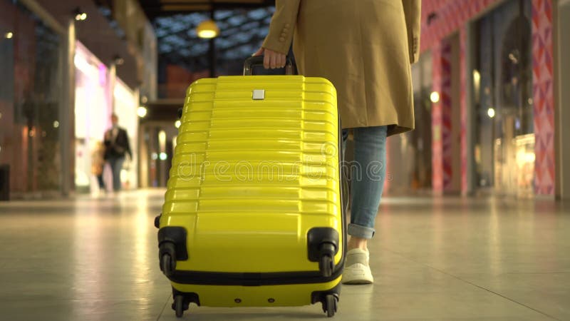 A young woman walks with a suitcase in the mall. Girl in a coat with a yellow suitcase.