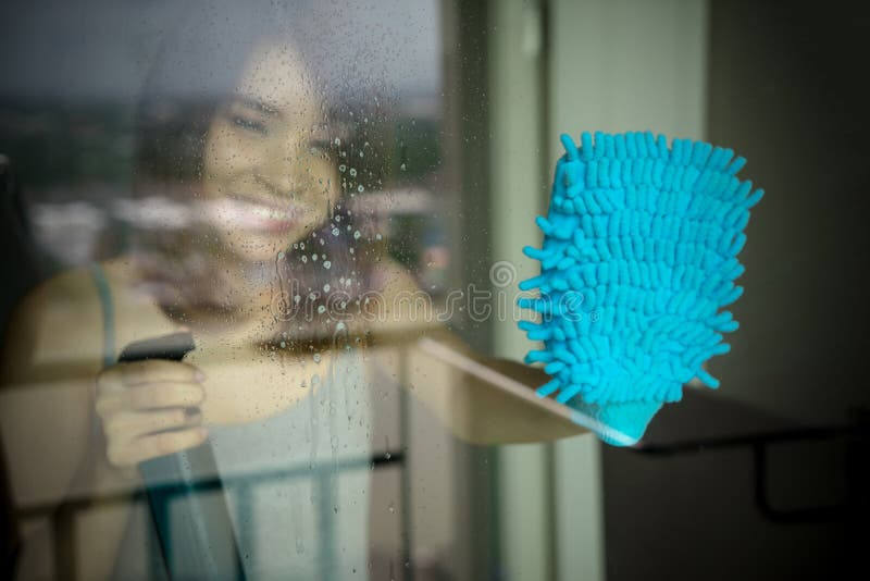 Young woman washing window. happy maid in gloves holding bottle royalty free stock photography