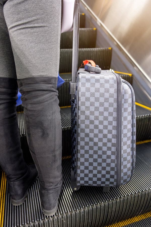 Young woman wear boot lower half with chess luggage standing on escalator at airport